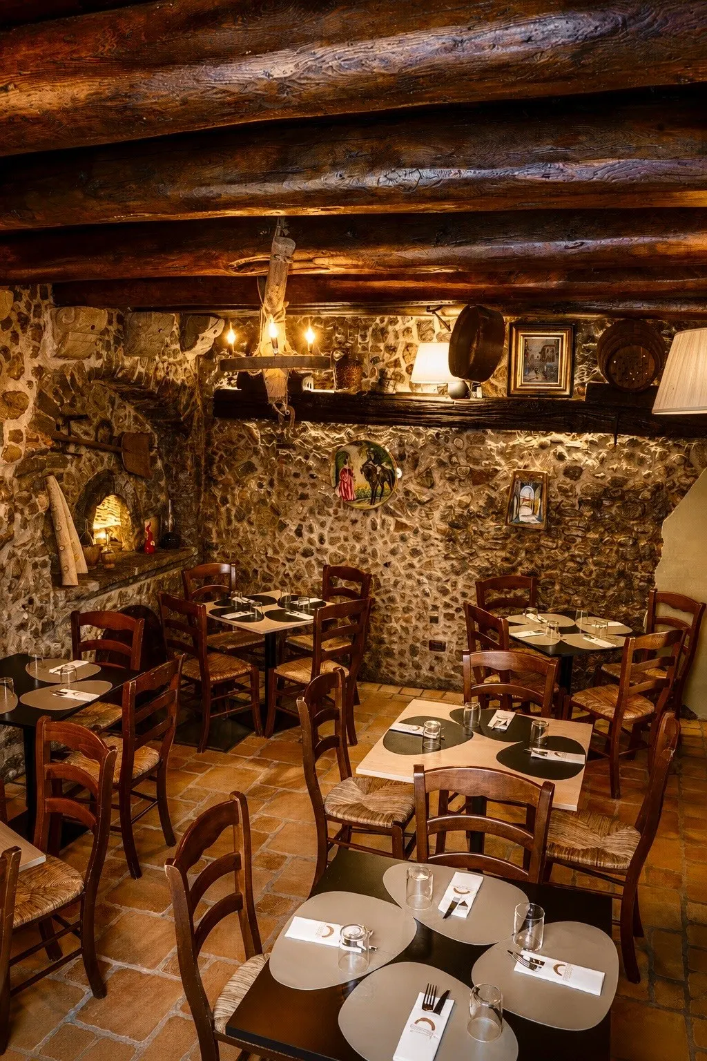 La sala dell'osteria: tavoli apparecchiati, travi in legno e muri in pietra